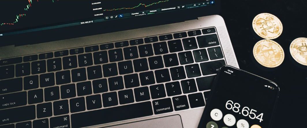 Laptop showing a crypto trading chart beside a smartphone calculator and Bitcoin coins, illustrating how Suncorp customers can buy cryptocurrency under Australia’s new AFSL rules.