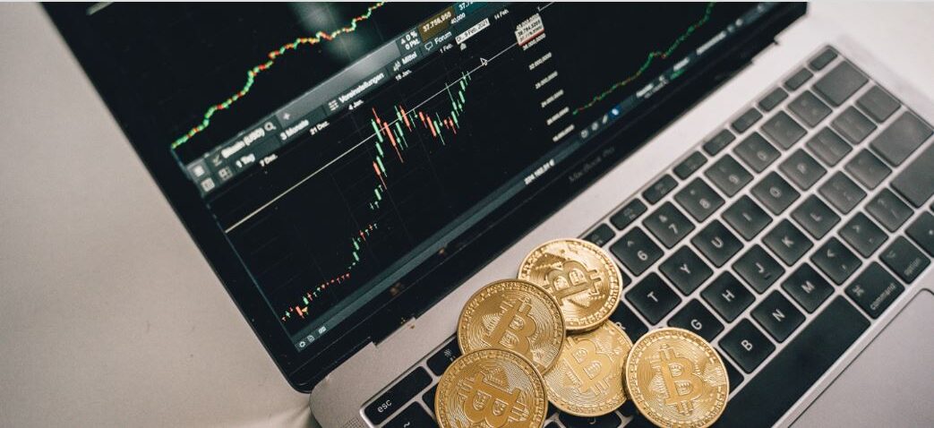 Can You Still Buy Crypto With TD Ameritrade headline displayed above a laptop with a cryptocurrency trading chart and Bitcoin coins.