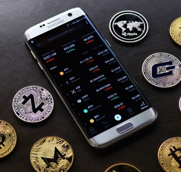 Can You Still Buy Crypto With Standard Bank in 2026 headline displayed beside a smartphone showing cryptocurrency prices surrounded by Bitcoin, XRP, Monero, and other crypto coins.