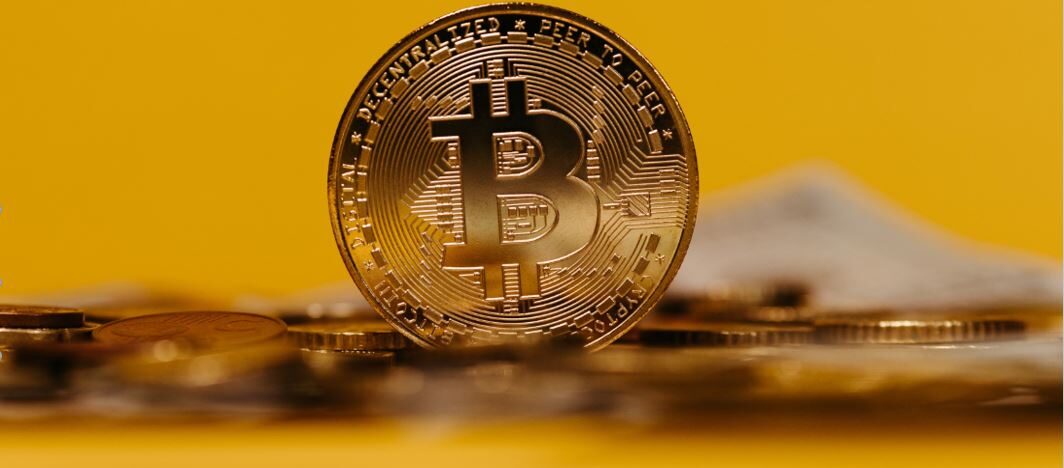 A close-up Bitcoin coin standing among scattered coins beneath the headline “Can You Buy Bitcoin With Western Union in 2026?”, illustrating the question of using Western Union to fund cryptocurrency purchases.